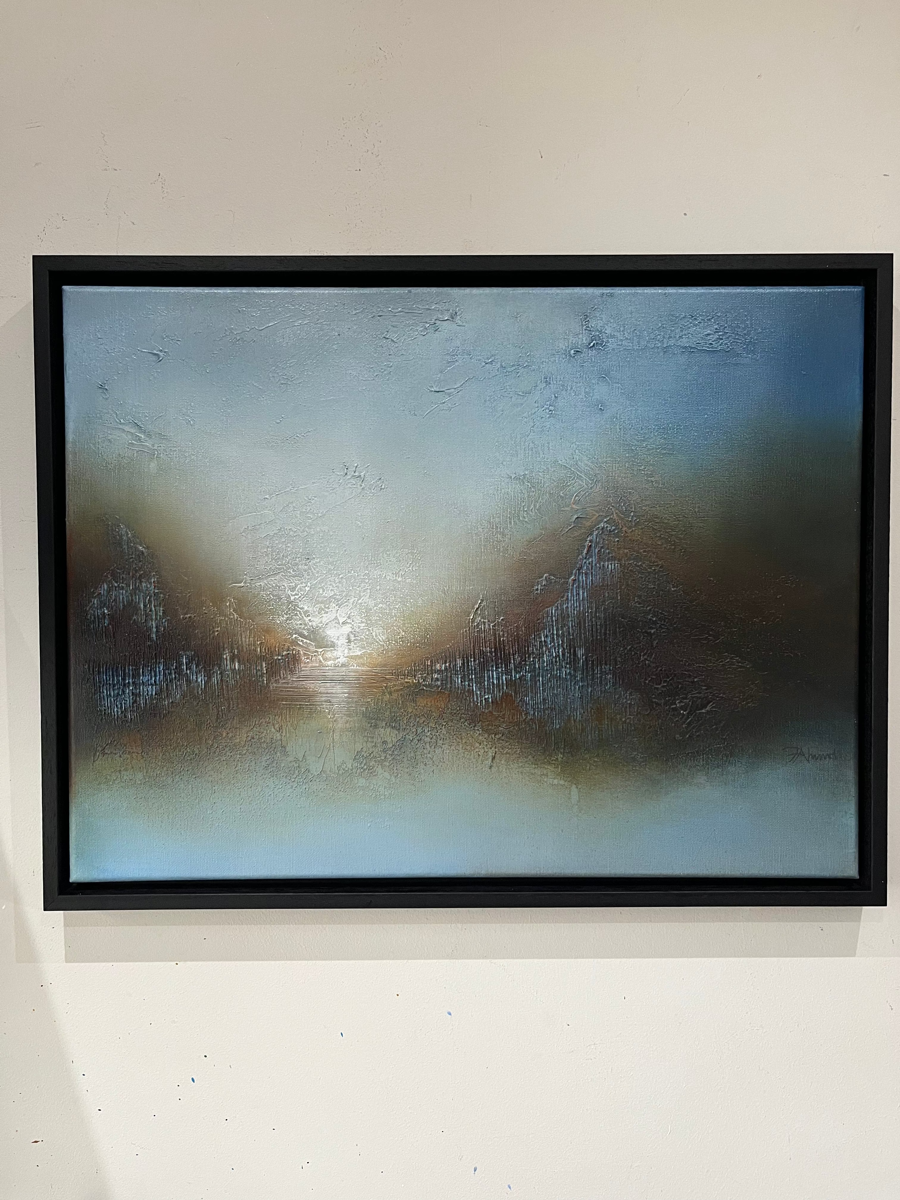 A framed abstract painting featuring textured brushstrokes of blue, gray, brown, and white, hung on a light beige wall.