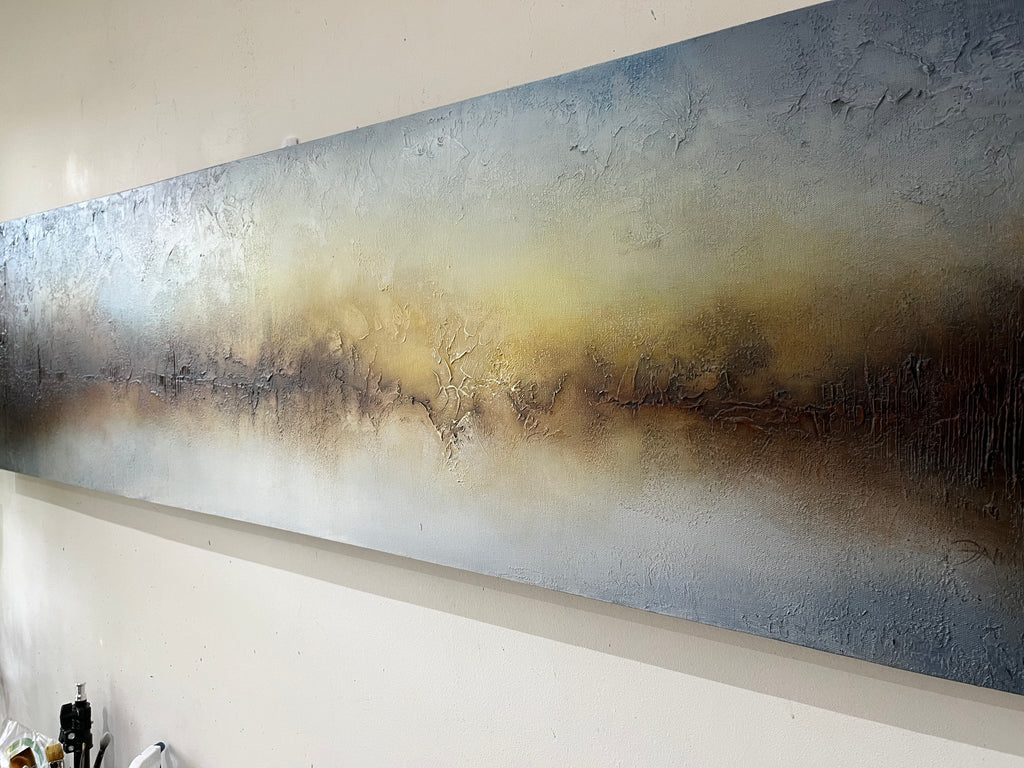 A large panoramic textured canvas painting mounted on a white wall, featuring a horizontal gradient of blue, gray, beige, and dark brown tones.