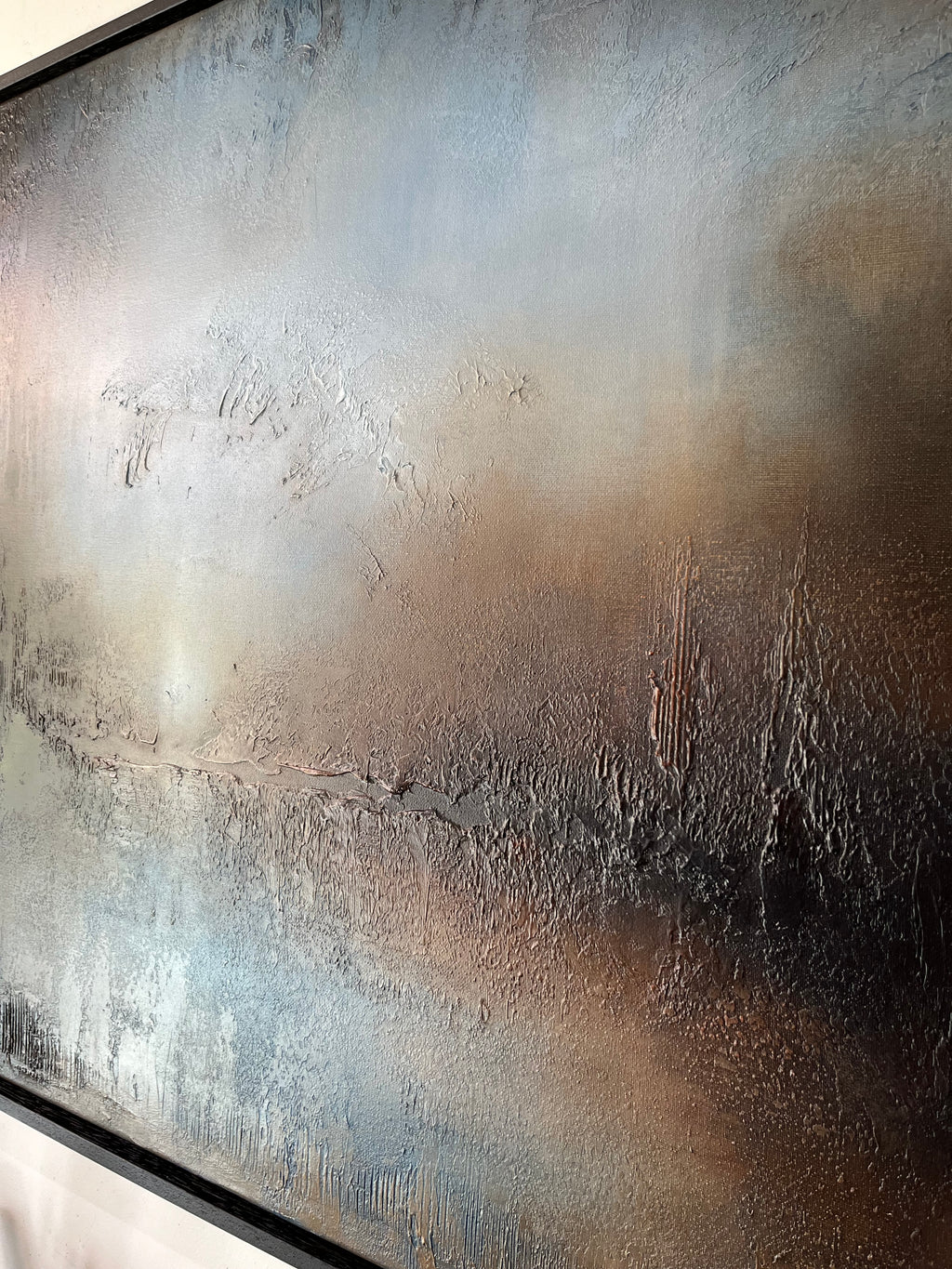 Abstract textured wall art featuring blended tones of gray, brown, beige, and black with a dark frame visible along the bottom edge.