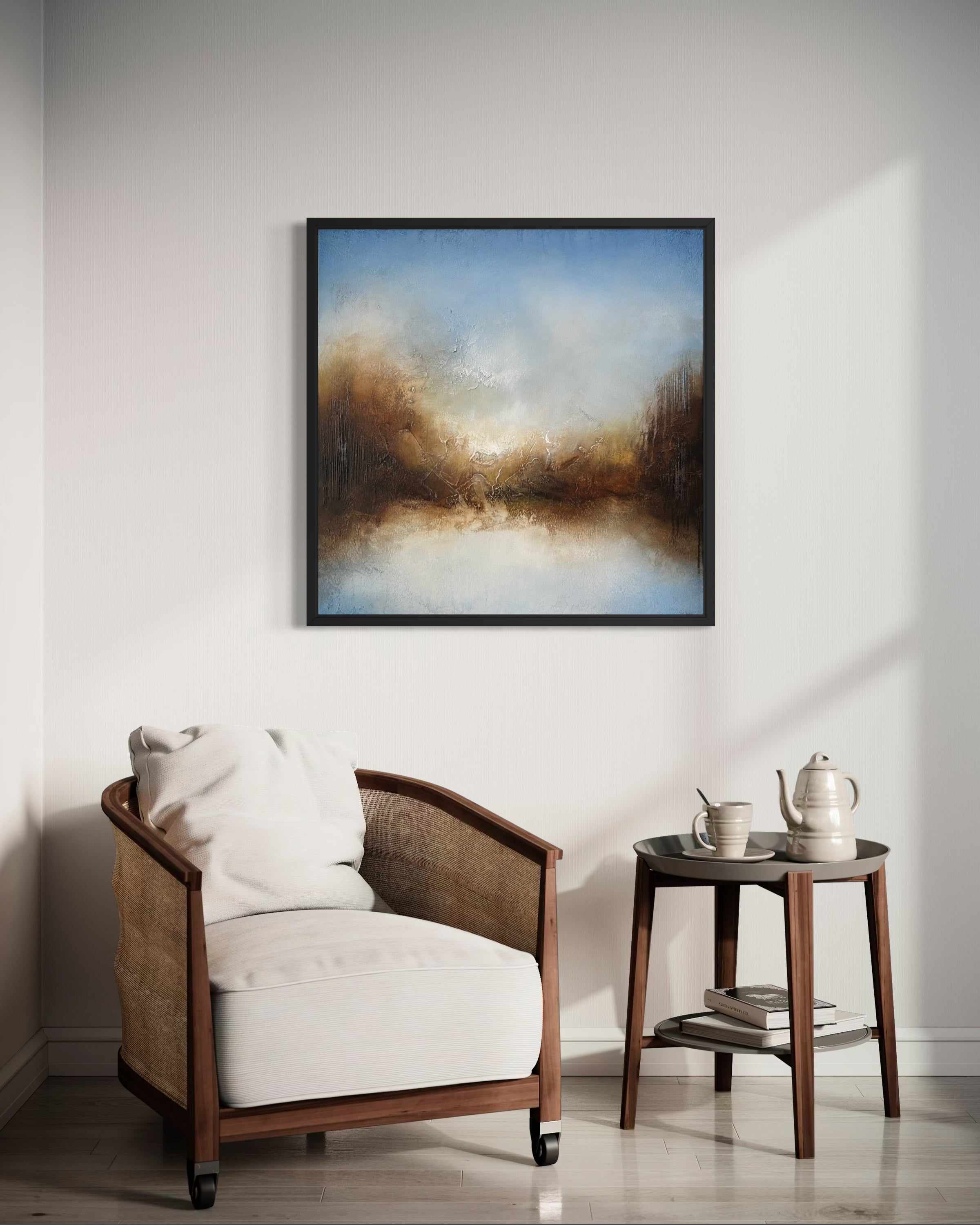 A framed abstract landscape painting hangs on a light gray wall above a wooden armchair and a small side table in a styled interior room.